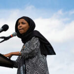 Woman in hijab speaking at podium with microphones.