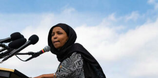 Woman in hijab speaking at podium with microphones.