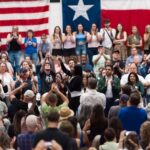 A large crowd at a political rally with people cheering and taking photos
