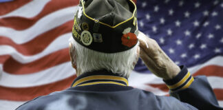 Veteran saluting in front of American flag.