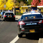 Police cars and school buses on a sunny street.