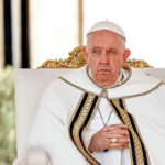 Elderly man in white robe sitting on chair.
