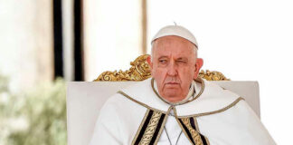 Elderly man in white robe sitting on chair.