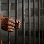 Hands gripping prison cell bars tightly.