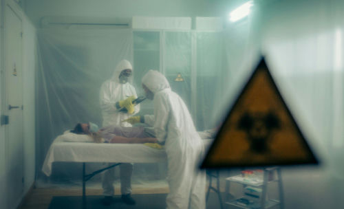 Two scientists examining a patient with biohazard sign visible.