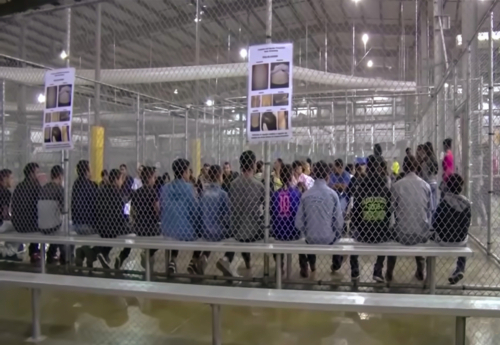 A group of young individuals seated in a detention center surrounded by security fencing and informational posters