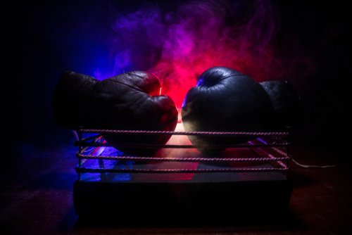 shutterstock_1375528124.jpg Two boxing gloves positioned in a ring with dramatic lighting and smoke