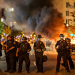 Teen Takeover CHAOS: Flamethrowers AND Fireworks! Police officers in riot gear facing a chaotic protest scene with smoke and fire