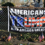 Americans for Trump banner on a fence with flags