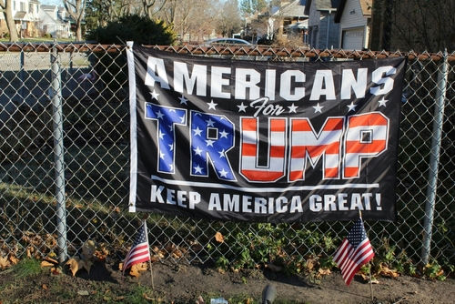shutterstock_2234961503 Americans for Trump banner on a fence with flags
