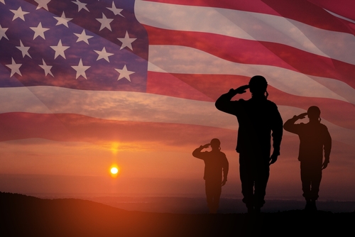 Silhouetted soldiers saluting against an American flag backdrop during sunset