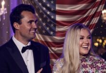 A smiling couple in formal attire standing in front of an American flag backdrop