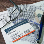 Medicare card with cash, documents, glasses, and pen.