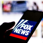 Silhouette hand holding phone displaying Fox News logo.