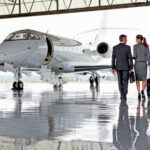 Gourmet GORGING on Taxpayer Dime — LOOK WHO! Two businesspeople walking towards a private jet in hangar.