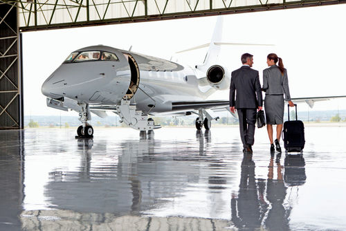 Two businesspeople walking towards a private jet in hangar.