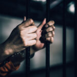 Hands gripping prison bars, suggesting confinement