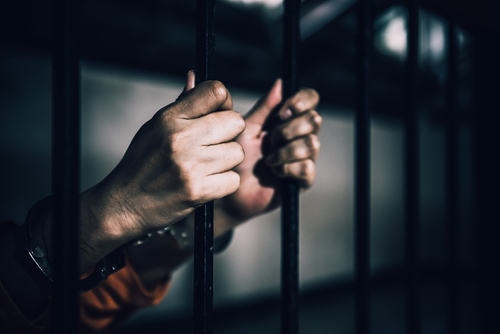 Hands gripping prison bars, suggesting confinement