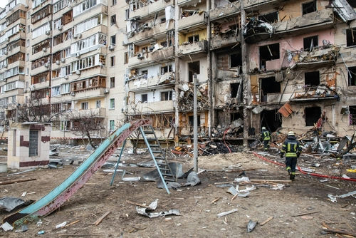 Damaged apartment building with debris scattered firefighters present.