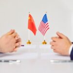 Two hands of individuals facing each other with flags of China and the USA on the table