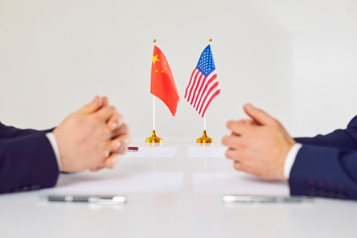Two hands of individuals facing each other with flags of China and the USA on the table