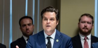 A man in a suit speaking at a conference table with others in the background