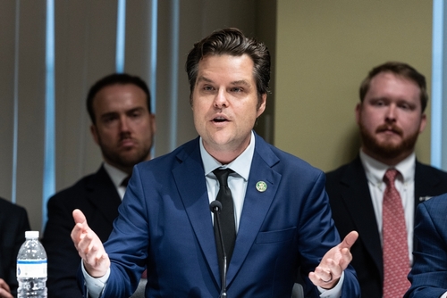 A man in a suit speaking at a conference table with others in the background