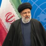 An Iranian political leader standing in front of the Iranian flag at a conference