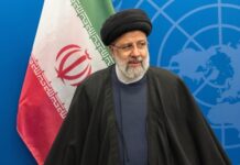 An Iranian political leader standing in front of the Iranian flag at a conference