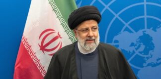 An Iranian political leader standing in front of the Iranian flag at a conference