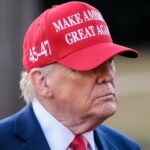 A man wearing a red cap with a political slogan, looking serious