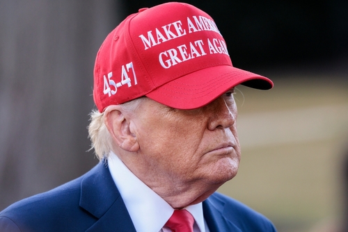 A man wearing a red cap with a political slogan, looking serious