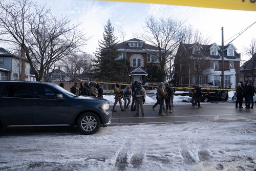 Law enforcement officers in tactical gear at a crime scene surrounded by police tape