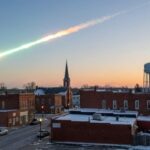 Mystery Boom Shocks HOMES — Then This… A meteor streaking across the sky above a small town at sunset