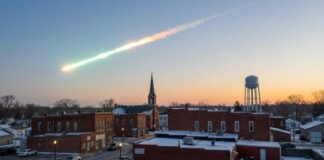 A meteor streaking across the sky above a small town at sunset