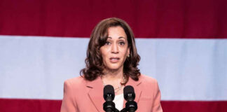 Woman speaking at podium with American flag background.