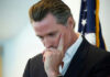 Man in suit thinking with hand on face near a U.S. flag