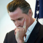 Man in suit thinking with hand on face near a U.S. flag