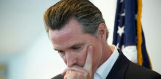 Man in suit thinking with hand on face near a U.S. flag