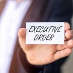 Federal Court Defies SCOTUS, Halts Trump Firings! Hand holding a small card with bold text in front of a blurred suit jacket