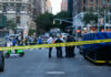 Police officers behind yellow crime scene tape on city street.