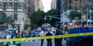 Police officers behind yellow crime scene tape on city street.