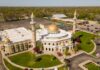 Aerial view of a mosque with golden domes and minarets surrounded by greenery