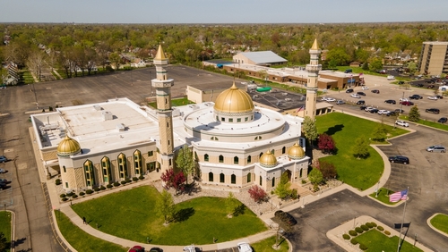 Aerial view of a mosque with golden domes and minarets surrounded by greenery