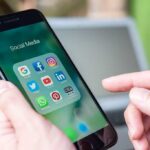 Person holding smartphone with social media app folder open