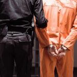 Prisoner in orange jumpsuit handcuffed with guard standing beside