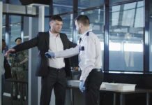 airport security officer patting down a man at a metal detector