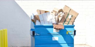 Blue dumpster overflowing with cardboard boxes
