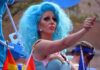 Dem Candidates Drag Queen OBSESSION Gets Weirder Drag performer with bright blue wig giving thumbs up at parade