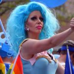 Dem Candidates Drag Queen OBSESSION Gets Weirder Drag performer with bright blue wig giving thumbs up at parade